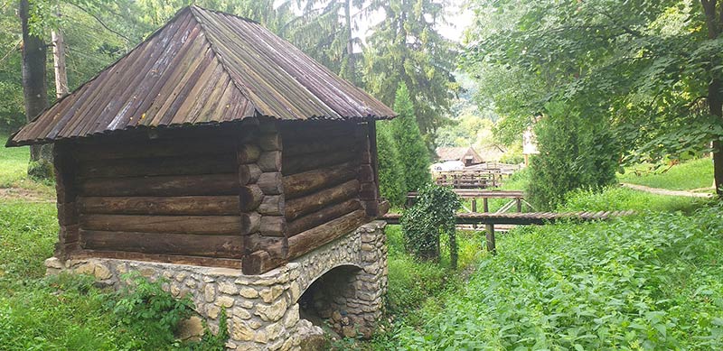 drvena kućica sa kamenom osnovom i drvenim mostićem u zelenilu